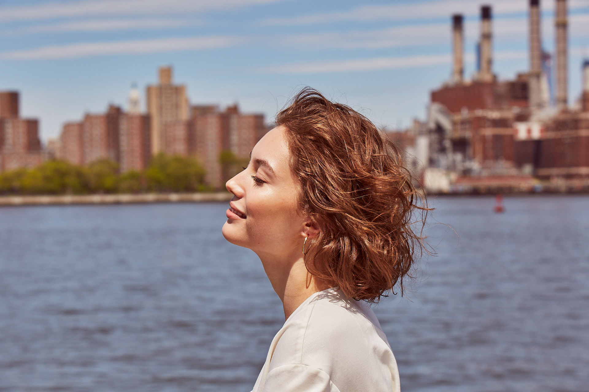 Side profile of a smiling woman in front of the water with background view of the city.