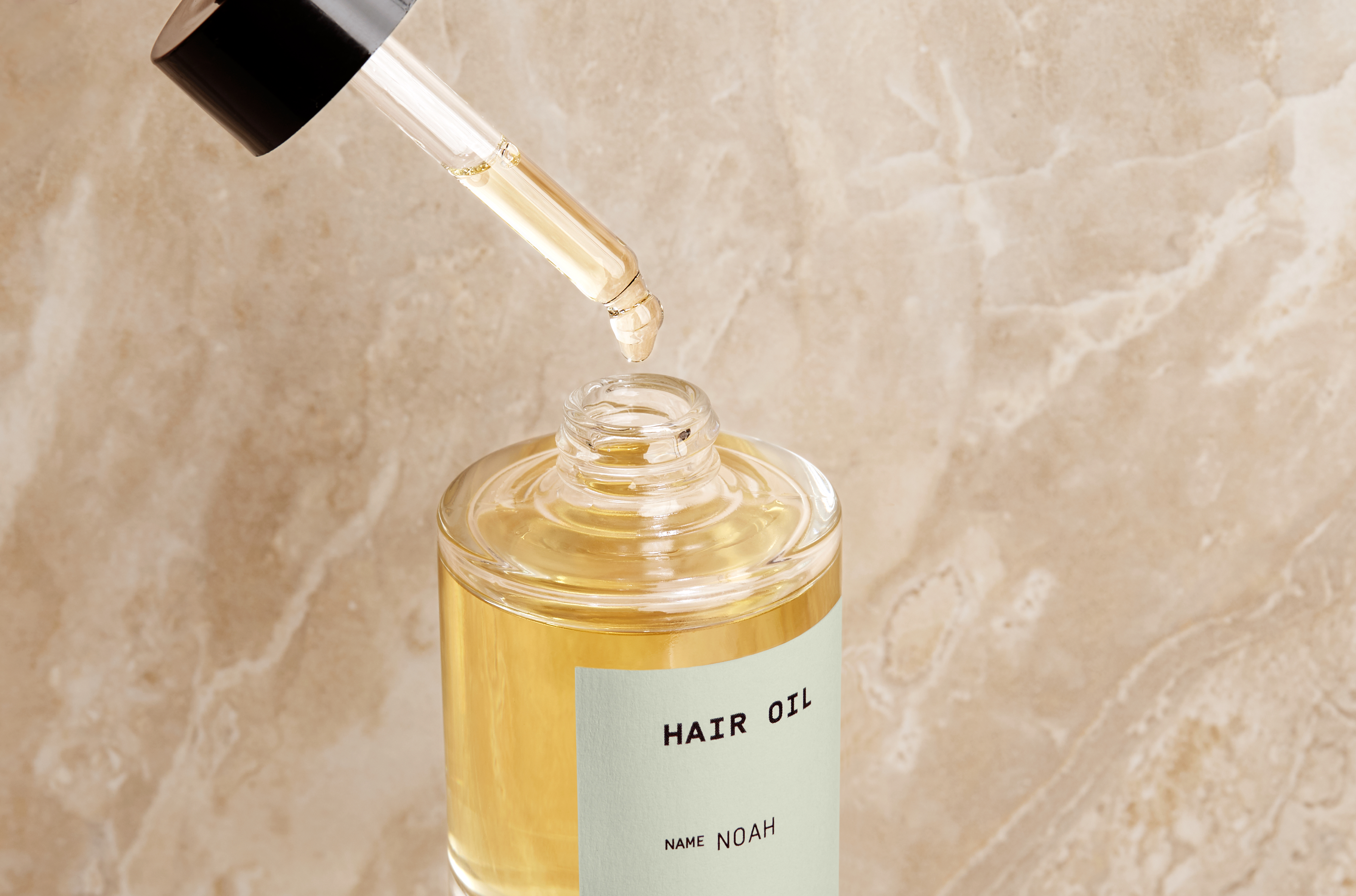 Custom hair oil in front of a marbled blush background