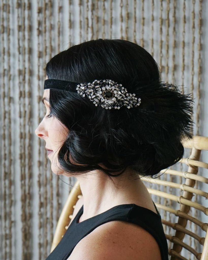 Side profile of a woman with short black curled hair and a feathered and embroidered black headband