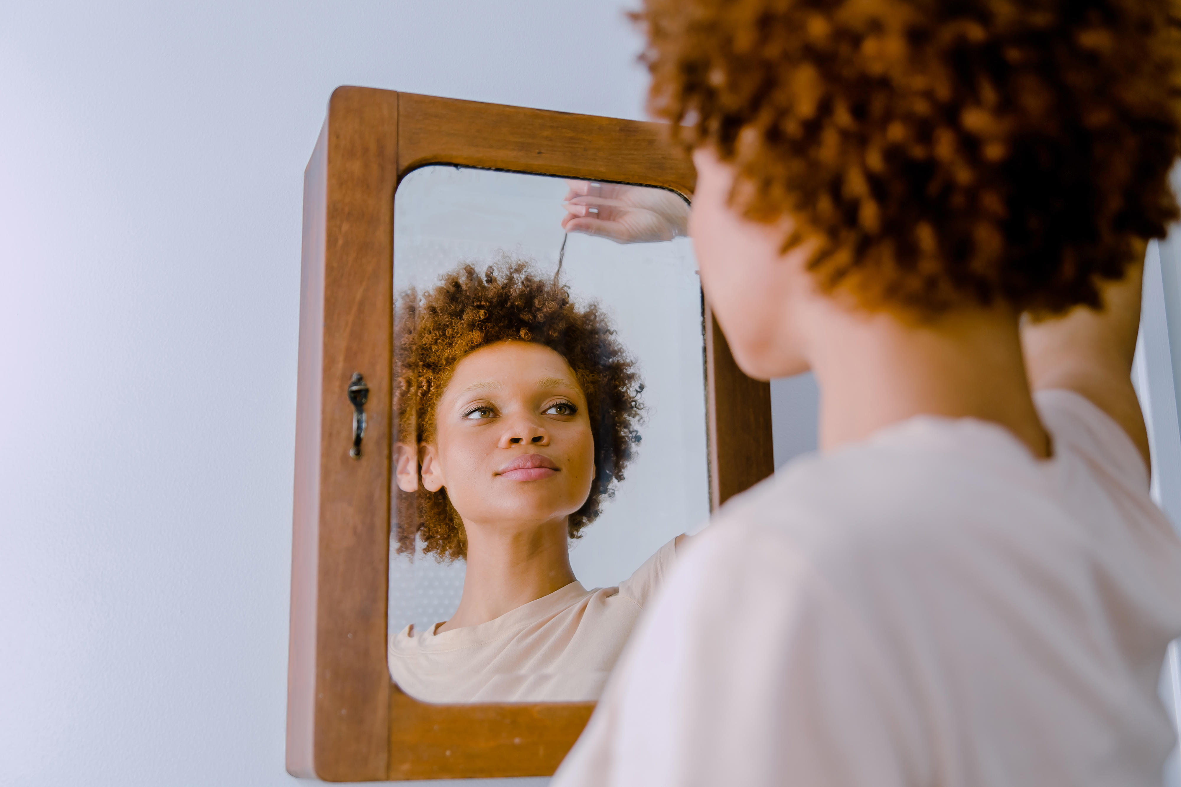 Curly haired woman staring at her reflection in the mirror examining her hair while pulling on one of her strands