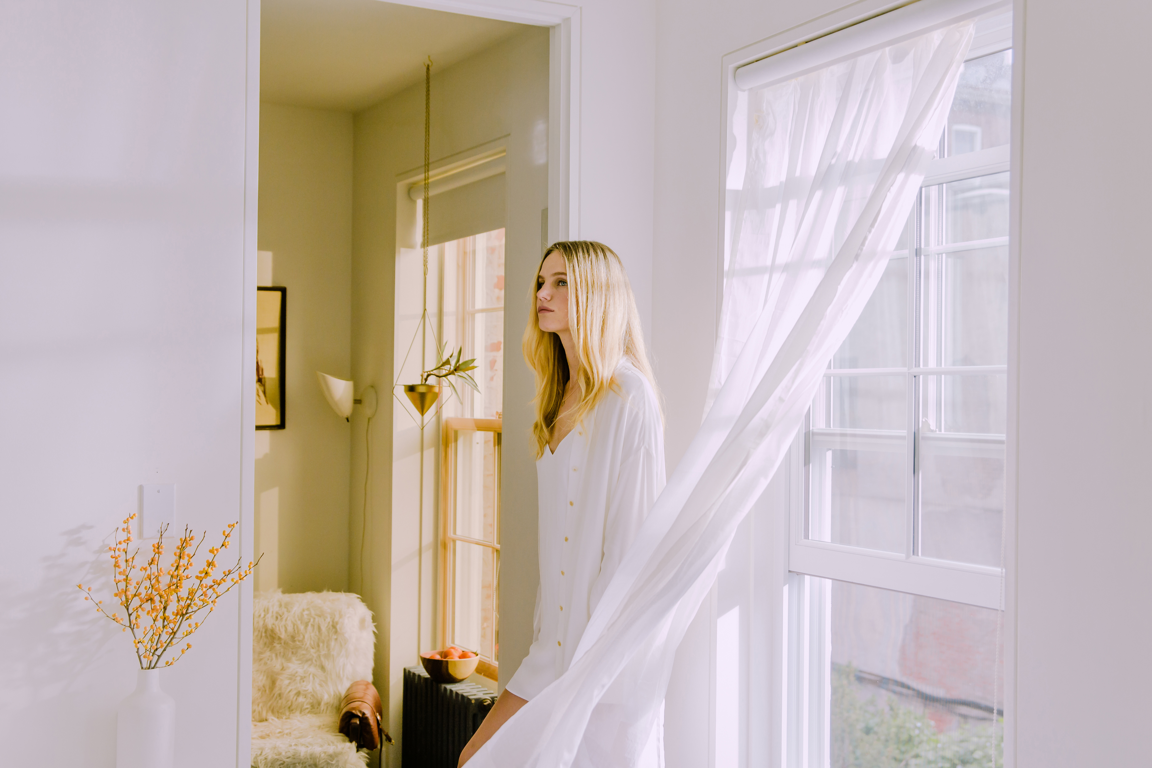 Blonde woman standing in her living room in front of a bright open window
