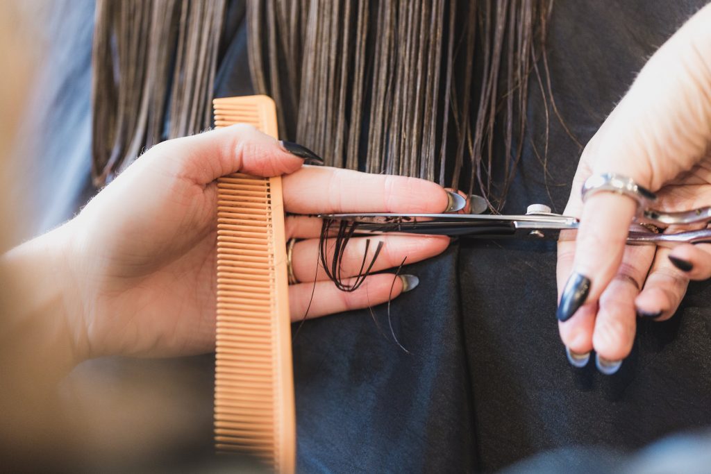 The hands of a woman cutting someones hair with a comb in one had and scissors in the other