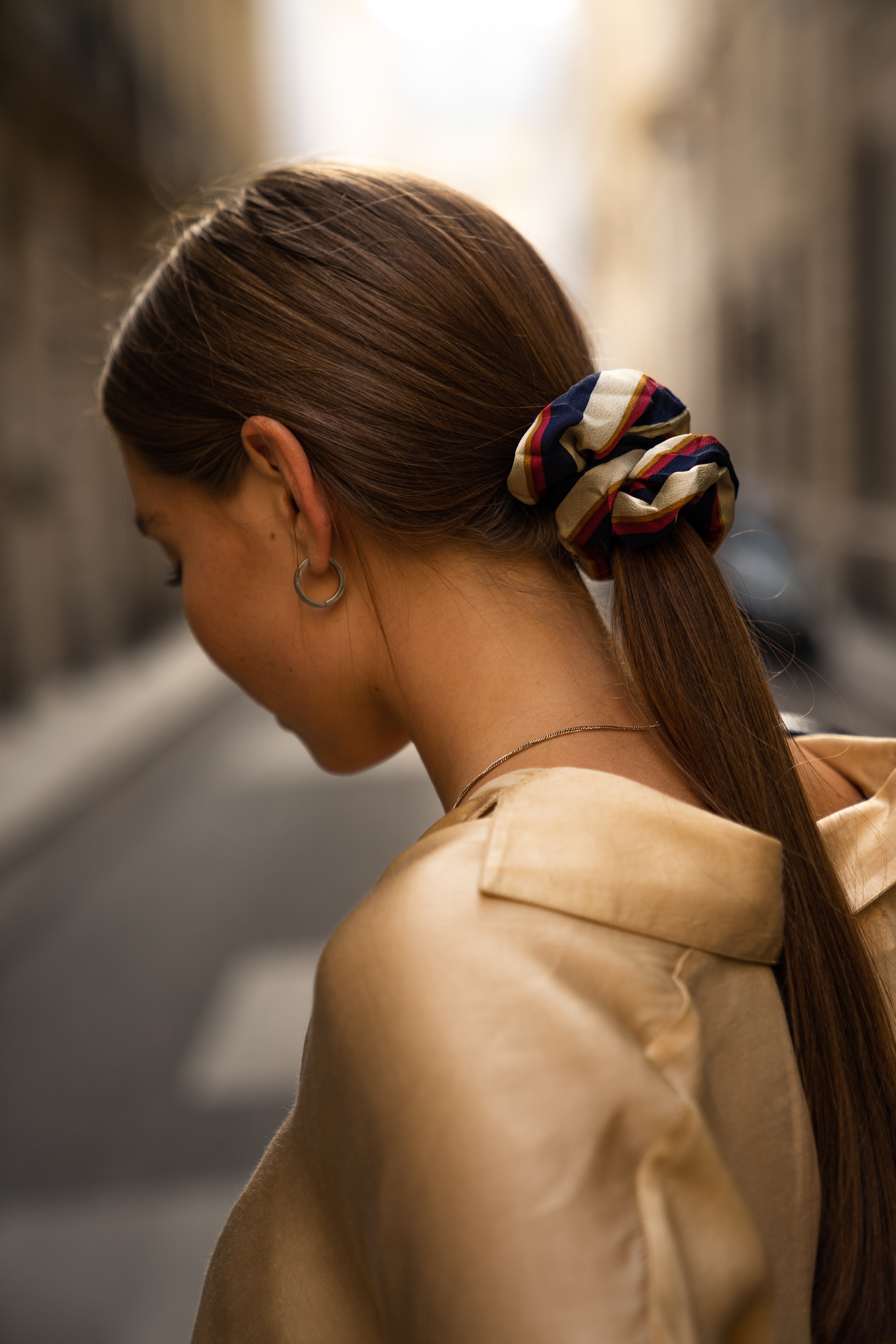 Girl with a long straight ponytail looks down with a striped scrunchie in her hair