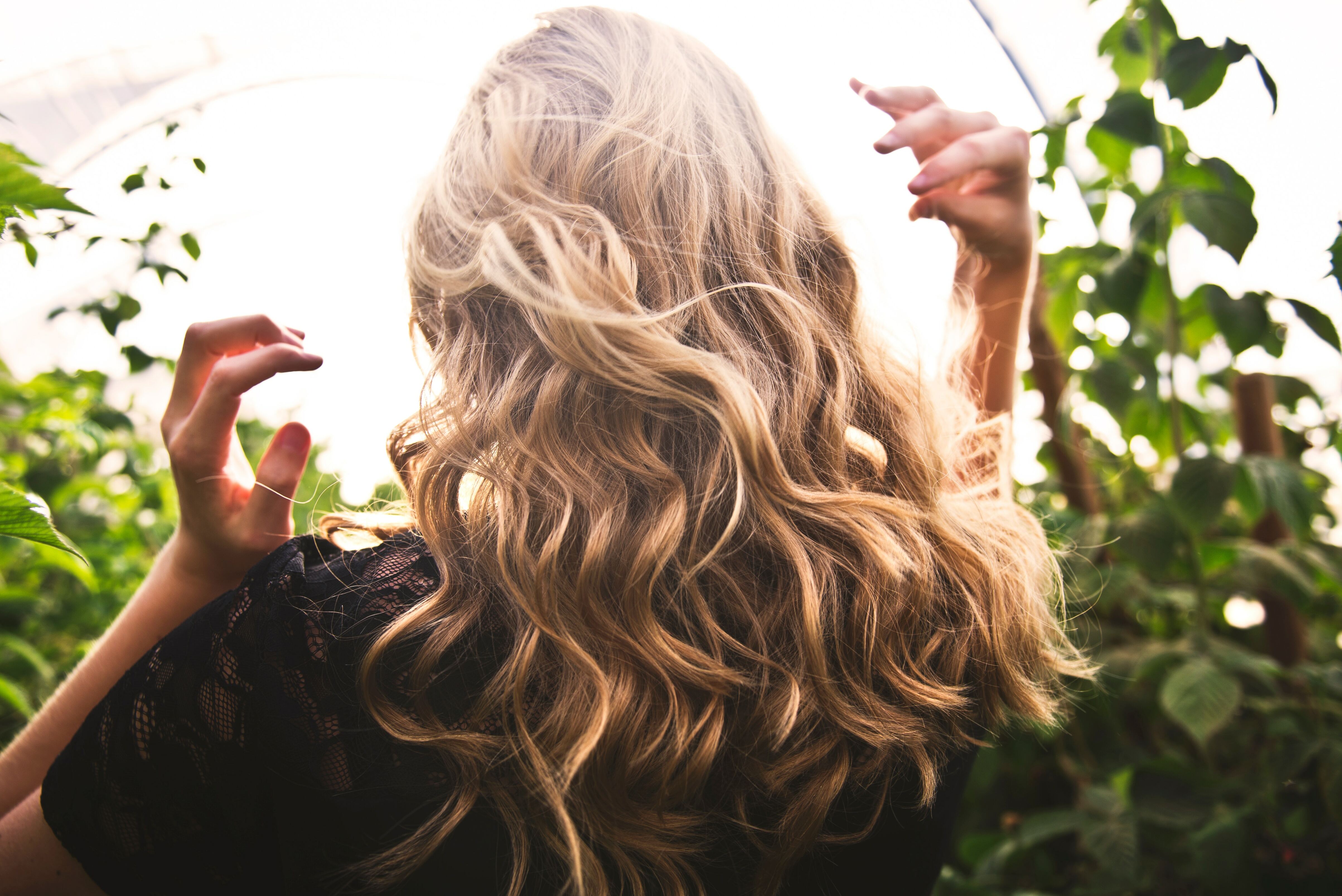 Back of woman's head with blonde hair surrounded by greenery