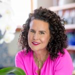 naturally curly founder michelle breyer poses with her dark, curly hair in a hot pink top