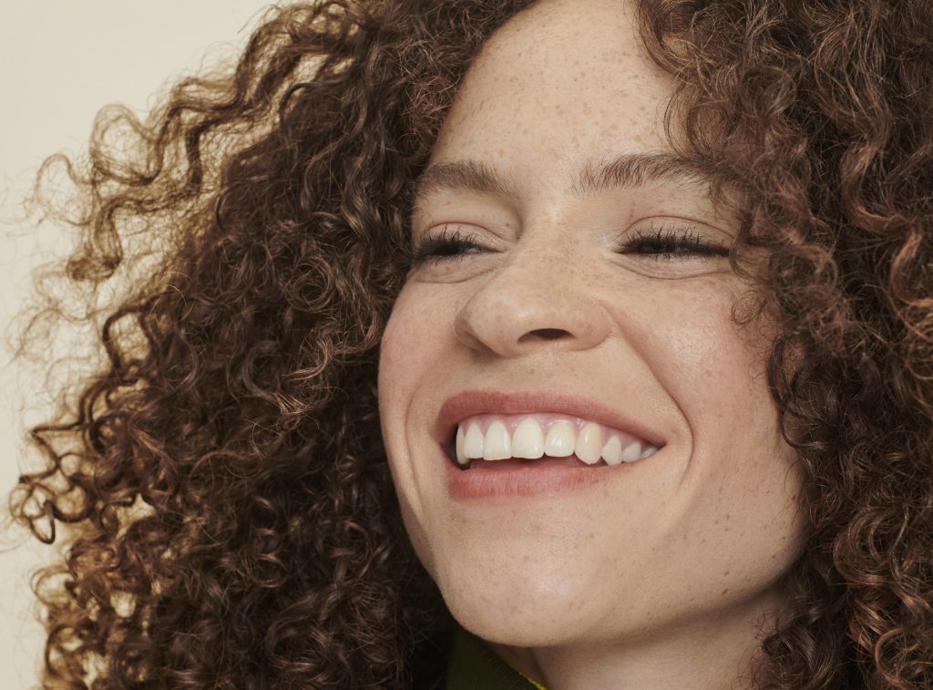 woman with brown, curly hair smiles