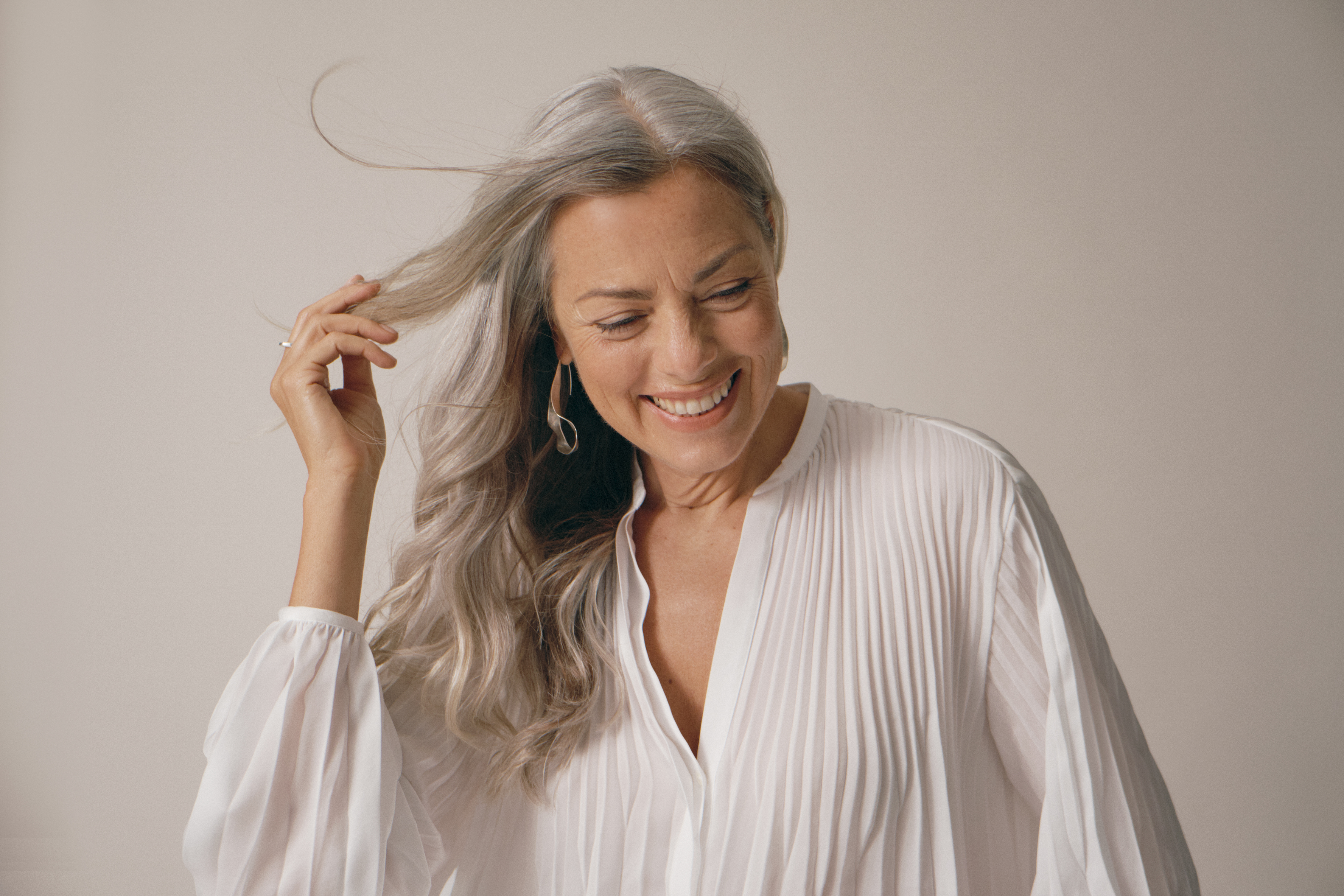 woman with white hair wears a flowing, white blouse and smiles