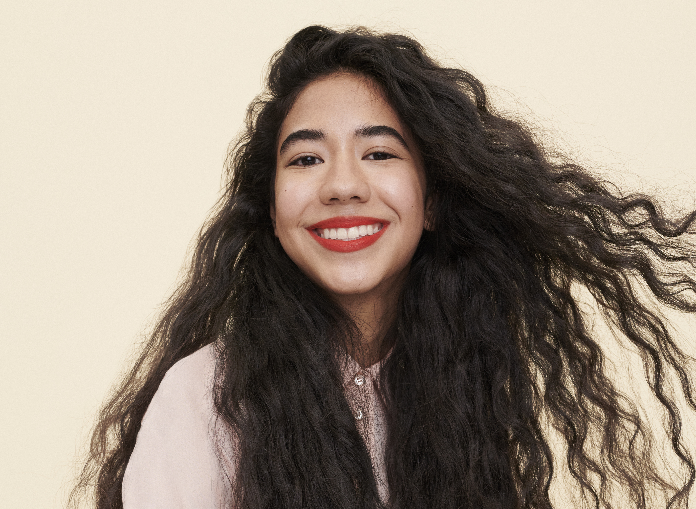 girl with long, brown curly hair smiles while wearing red lipstick