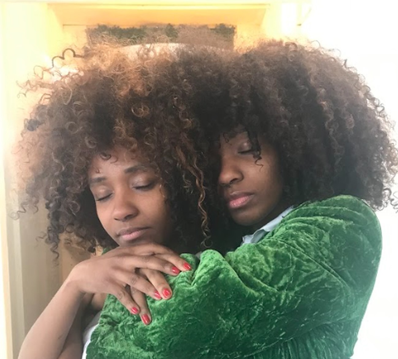 twin women with brown, curly hair embrace each other