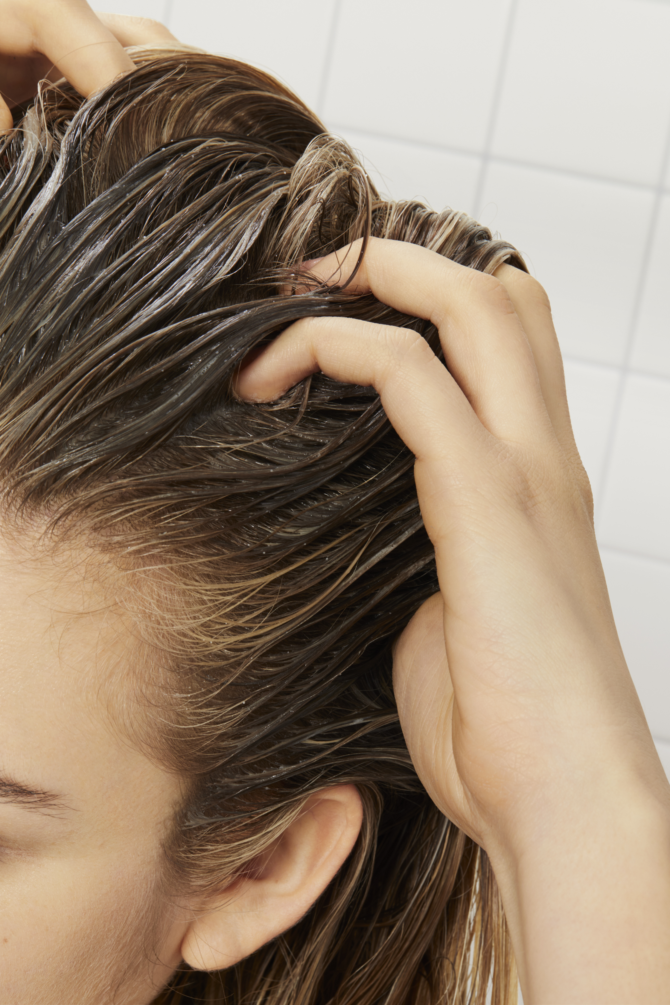 woman with dark, blonde hair giving herself a scalp massage