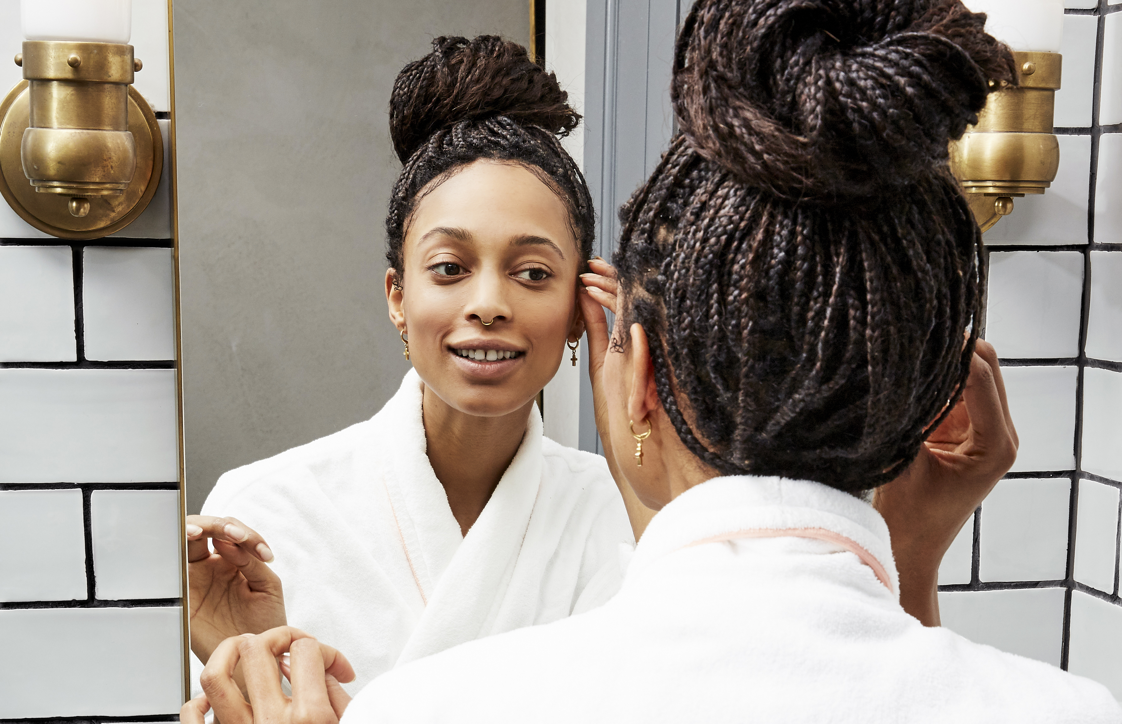 woman with braids smiles into her bathroom mirror