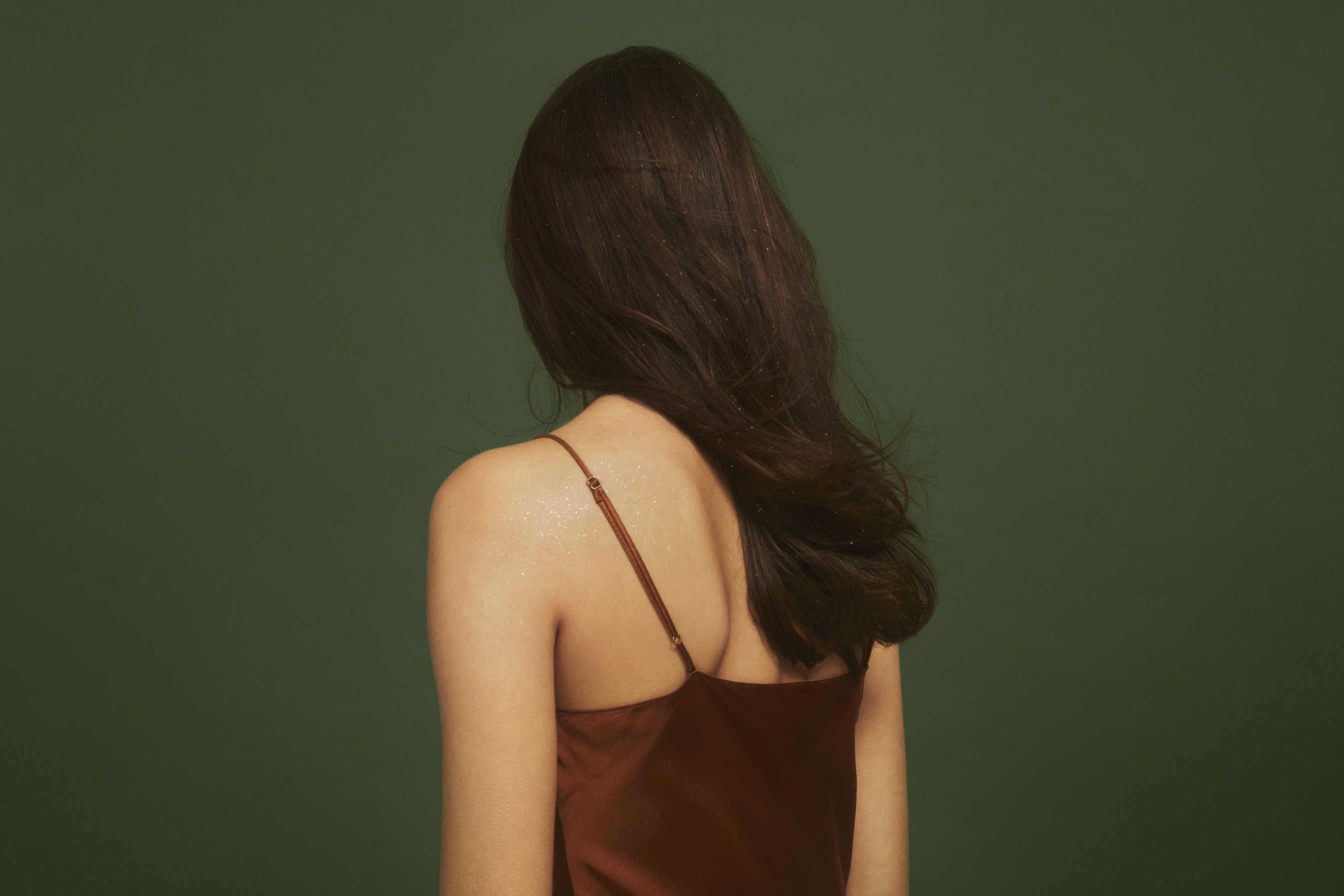 woman with long, brown hair stands against a dark, green backgorund
