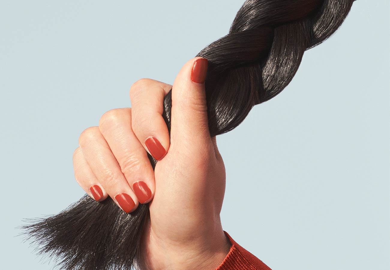 woman with red nails holding onto her long, dark, braided hair