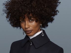 Curly haired woman poses in front of a blue background