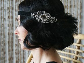 Side profile of a woman with short black curled hair and a feathered and embroidered black headband