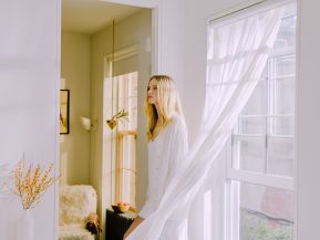 Blonde woman standing in her living room in front of a bright open window