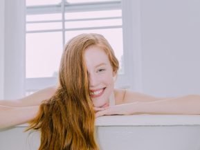 Long ginger haired woman in a bathtub smiling