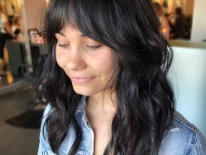 woman with black hair and curtain bangs smiles in a hair salon