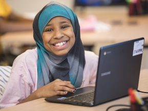 young girl smiles while working on a computer