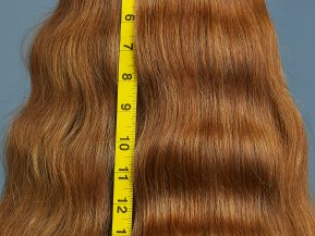 woman with red, wavy hair shows off her long hair next to measuring tape