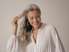 woman with white hair wears a flowing, white blouse and smiles